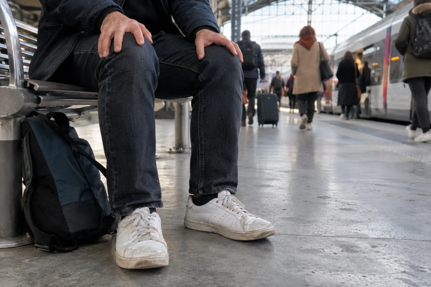 Sur un quai de gare, une personne assise pose les deux pieds bien à plat au sol et appuie les mains sur ses cuisses.