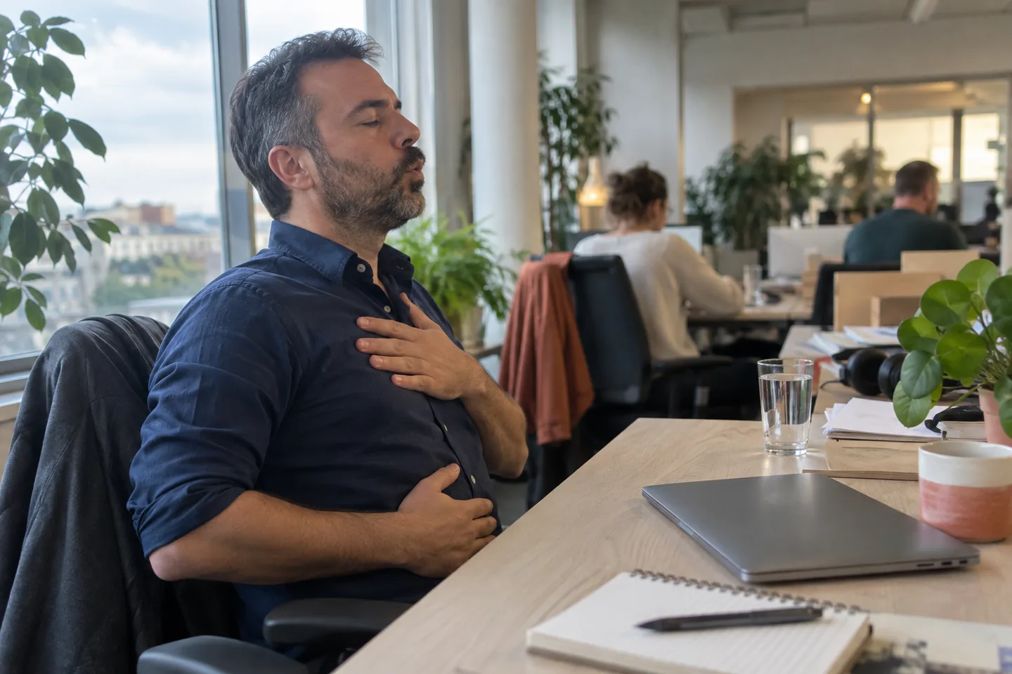 Un homme assis à son bureau, une main sur le ventre et l’autre sur la poitrine, souffle doucement par la bouche.