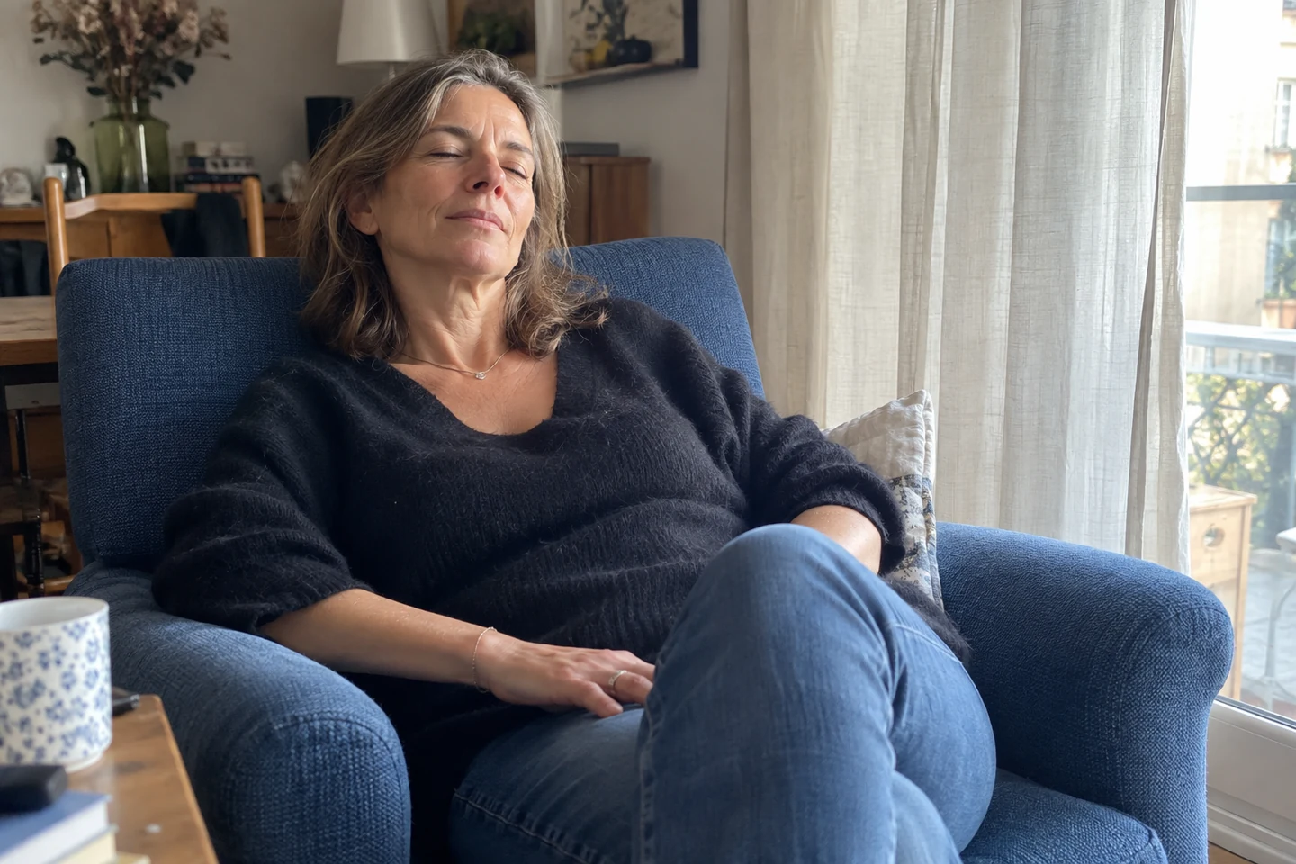 Une femme se repose dans un fauteuil près de rideaux clairs.